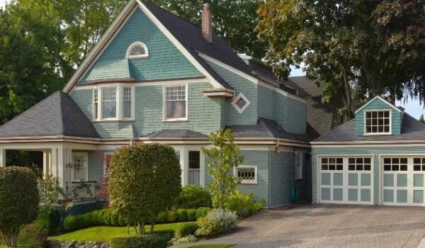 Freshly painted traditional home exterior featuring soft blue siding, crisp white trim, and a well-maintained garage, surrounded by mature landscaping.