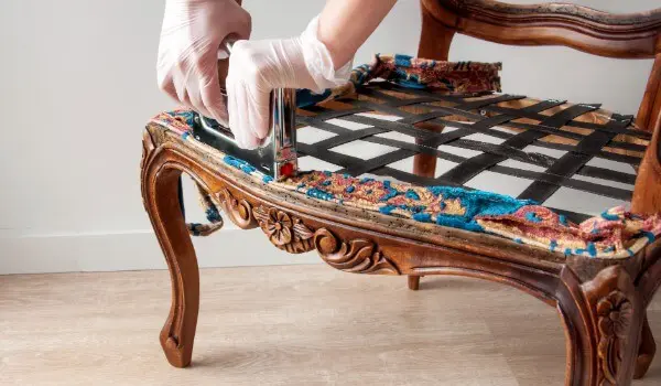 Furniture restoration process showing gloved hands carefully removing old upholstery from a wooden chair frame in preparation for refinishing or repair.